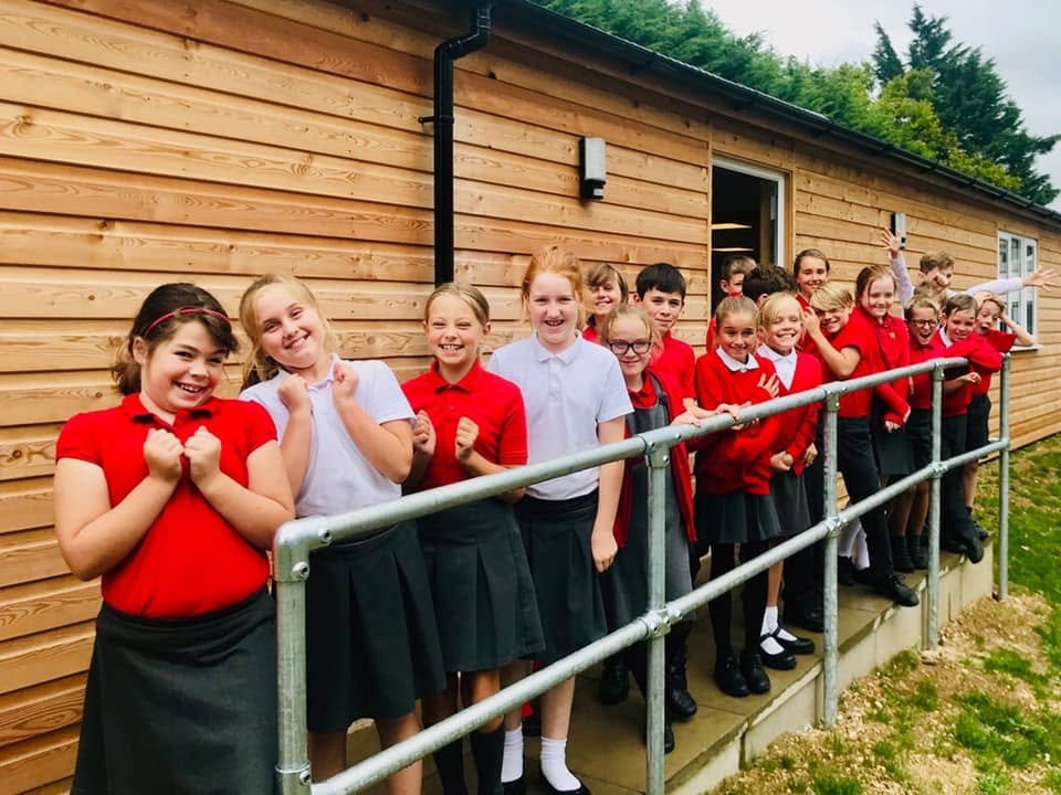 Children from the village primary school smiling along the rail outside the timber-clad Community Clubhouse