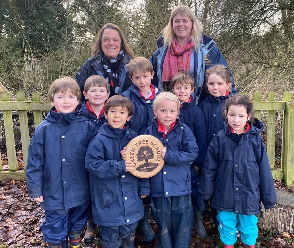 Young children holding a Woodland Trust Green Tree School gold award outdoors